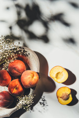flat lay with ripe peaches in metal bowl with gypsophila flowers on light marble surface with...