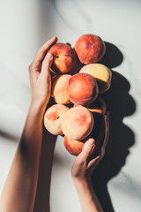 cropped shot of woman holding fresh and ripe peaches on light marble surface