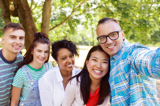 people, friendship and international concept - happy smiling young woman and group of happy friends taking selfie outdoors