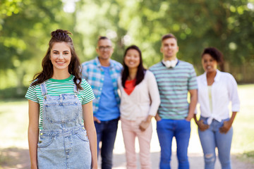 people, friendship and international concept - happy smiling young woman and group of happy friends outdoors