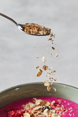 oat flakes in a spoon over a red smoothie in a pial on a concrete background