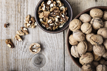 Fototapeta na wymiar Walnut kernels in a bowl and whole walnuts on table.