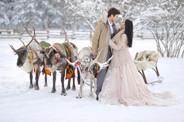 Fototapeta na wymiar Winter wedding European bridegroom and Asian bride with a harness of reindeer