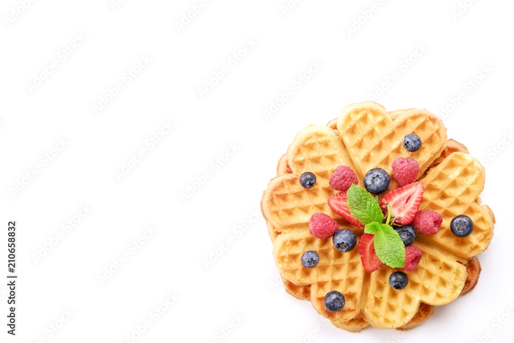 Wall mural Heart shape belgium waffles with assorted berries mix, strawberry, blueberry, raspberry and red currant decorated with mint leaf on white ceramic plate. Close up, copy space, background, top view.