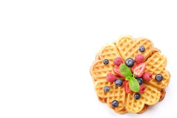 Heart shape belgium waffles with assorted berries mix, strawberry, blueberry, raspberry and red currant decorated with mint leaf on white ceramic plate. Close up, copy space, background, top view.
