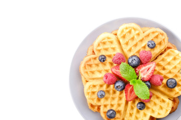 Heart shape belgium waffles with assorted berries mix, strawberry, blueberry, raspberry and red currant decorated with mint leaf on white ceramic plate. Close up, copy space, background, top view.