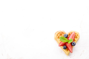 Heart shape belgium waffles with assorted berries mix, strawberry, blueberry, raspberry and red currant decorated with mint leaf on white ceramic plate. Close up, copy space, background, top view.