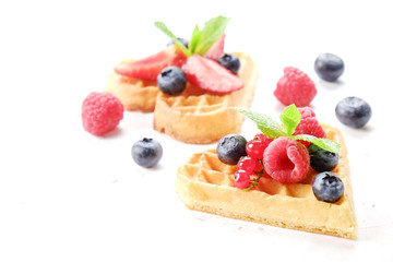 Heart shape belgium waffles with assorted berries mix, strawberry, blueberry, raspberry and red currant decorated with mint leaf on white ceramic plate. Close up, copy space, background, top view.