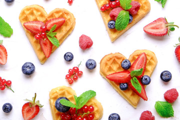 Heart shape belgium waffles with assorted berries mix, strawberry, blueberry, raspberry and red currant decorated with mint leaf on white ceramic plate. Close up, copy space, background, top view.