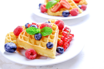 Heart shape belgium waffles with assorted berries mix, strawberry, blueberry, raspberry and red currant decorated with mint leaf on white ceramic plate. Close up, copy space, background, top view.