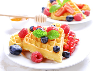 Heart shape belgium waffles with assorted berries mix, strawberry, blueberry, raspberry and red currant decorated with mint leaf on white ceramic plate. Close up, copy space, background, top view.