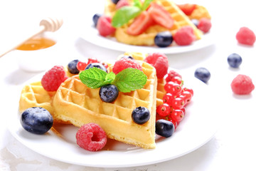 Heart shape belgium waffles with assorted berries mix, strawberry, blueberry, raspberry and red currant decorated with mint leaf on white ceramic plate. Close up, copy space, background, top view.