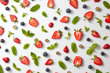 fruit pattern with half strawberries, blueberries and mint leaves on a white background, top view