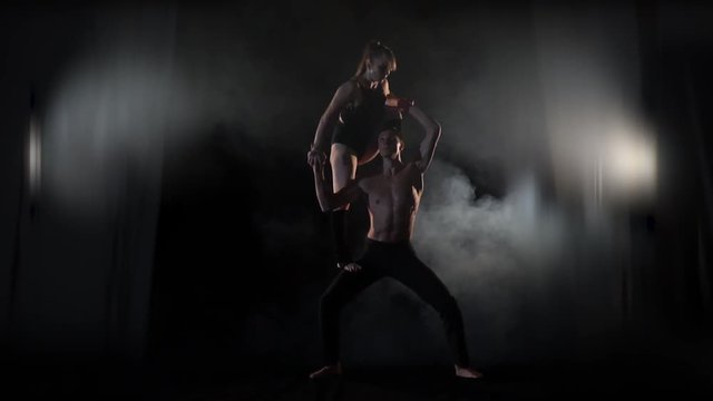 A couple in the smoke is engaged in acro yoga, a man supports a woman