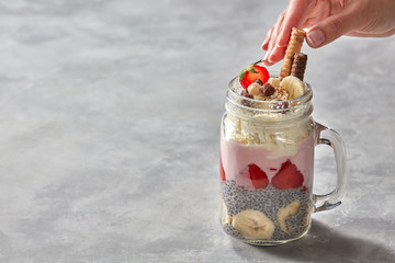 Healthy breakfast in the hand: yogurt parfait with chia pudding, strawberries and banana in glass on a stone background