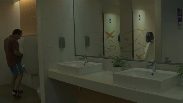 A man uses a urinal in the toilet of the airport