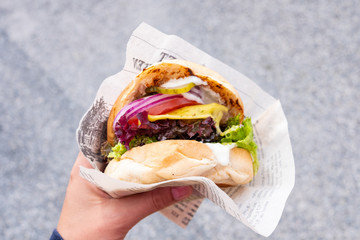 Hand of a young man holding an organic vegan burger with seitan patty in his hand during a street food festival - 210660219