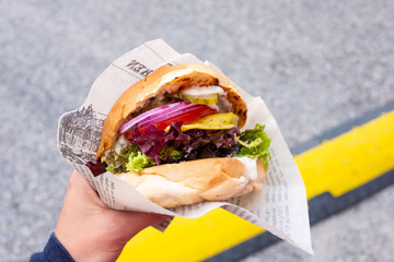 Hand of a young man holding an organic vegan burger with seitan patty in his hand during a street...
