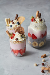Colorful layered smoothie with berries, biscuits and whipped cream in jar on a stone background