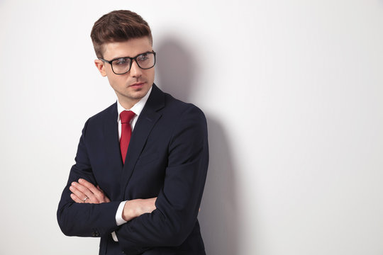 young businessman with glasses and arms folded looks to side