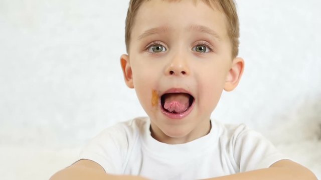 Close-up: a child looks and smiles at the camera at a slower pace. The child shows joy, shows the tongue and a broad smile, the baby's mouth is dirty with food