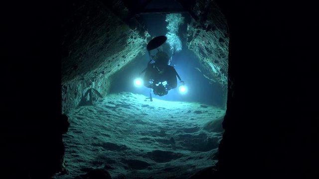 Scuba diver swims inside the wreck tunnel at nignight - Cousteau's precontinent 