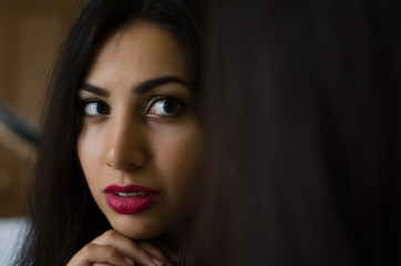 Fototapeta premium Young charming brunette girl looks at her reflection in the mirror