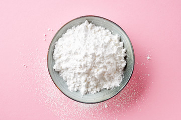 Bowl of powder sugar on white background, from above