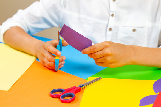 Child hands cutting colored paper with scissors at the table.