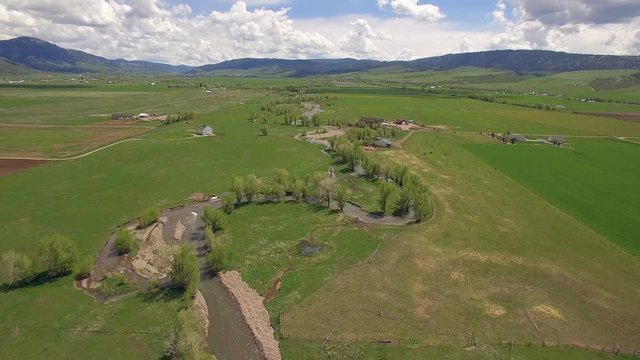 Aerial view flying backwards over river winding through green valley in Star Valley Wyoming getting closer to ground.