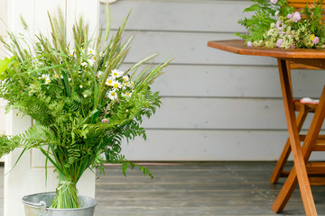 Festive bouquet of white yellow and purple, blue wildflowers, chamomile, herbs and flowers on wooden table, wooden house background. Birthday, Mother's, Women's, Wadding Day concept. Ligo, Latvia