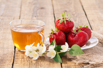 Glass cup of green tea and red ripe strawberries on glass saucer