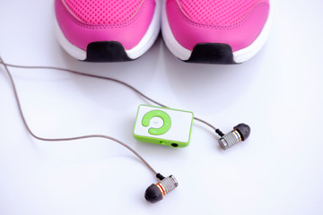 Pink running shoes for women and mp3 player with headphones on a white background