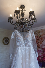 white bridal dress hangs on a beautiful chandelier. beautiful and charming white formal dress.