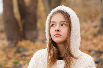 Close-up portrait of beautiful thoughtful dreaming little girl in white hoody coat staying in autumn forest, outdoors