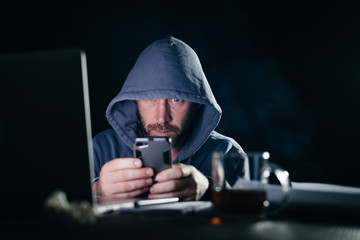 mysterious bearded man hacker in the hood sits in the dark, crack the password on the phone