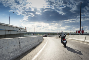 Back view of motorcycle driver driving in beautiful sunset. Clouds on the sky. Concrete barrier on the road