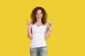 Horizontal shot of happy cheerful ginger young female has wide-open mouth on face, crosses fingers, has big dream, prays for good luck or success before passing college exams. Emotions, hope, faith