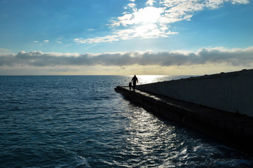 a person walks along the pier and leads the child's hand - around the sea and the blue sky with clouds