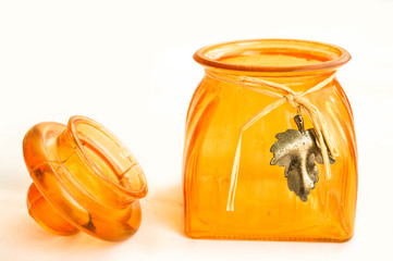 a small open glass orange jar with a lid and an iron sheet on a straw thread on a white background