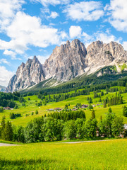 Rocky ridge of Pomagagnon Mountain above Cortina d'Ampezzo with green meadows and blue sky with...