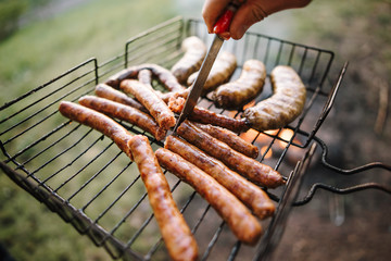 Fresh sausage and hot dogs grilling outdoors on a gas barbecue grill.