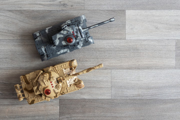 Two toy tanks on a gray, wooden surface