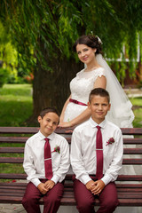 Gorgeous young bride with younger brothers posing at camera, at her wedding day. Family photo.