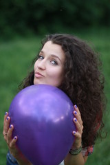 Naklejka premium A young woman is holding a purple balloon in her hands. Young woman with dark curly hair. Young woman on a green background