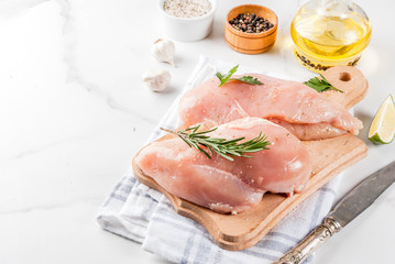 Raw meat, chicken breast filet, with olive oil, herbs and spices on white marble background, copy space