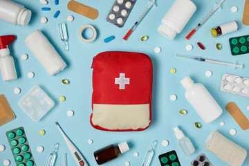 top view of red first aid kit bag on blue surface surrounded with different medicines