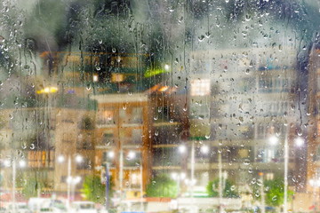 Fondo abstracto de ciudad a través de la ventana.Noche lluviosa y calles de la ciudad. Gotas de lluvia en el cristal