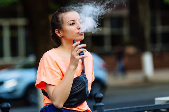 Pretty young hipster woman vape ecig, vaping device at the sunset. Toned image.