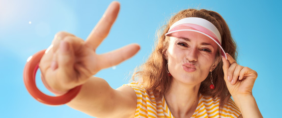 happy healthy woman against blue sky showing victory gesture